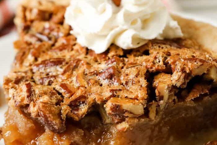 A slice of pecan pie with whipped cream and pecans
