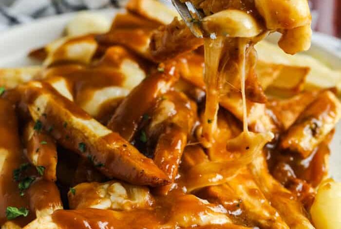 fork full of Poutine with plate full behind it