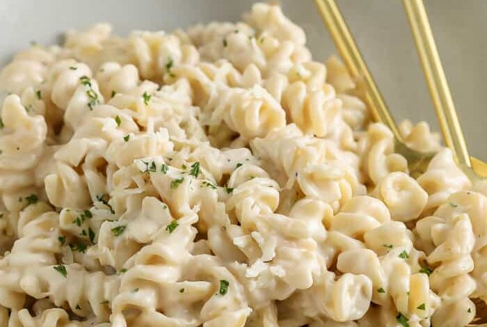 creamy garlic pasta in a bowl with gold coloured utensils