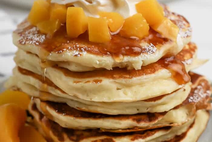 stack of yogurt pancakes topped with peaches and whipped cream