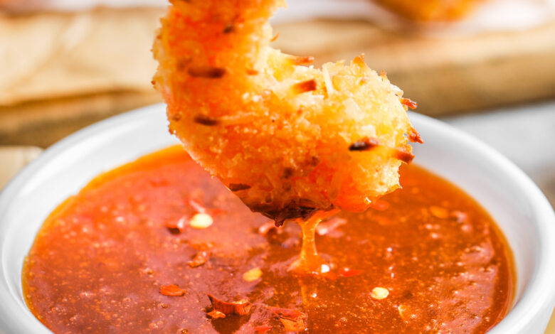 A breaded shrimp being dipped in a bowl of sweet chili sauce