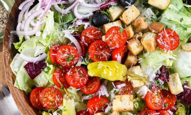 An Italian salad in a wood bowl with dressing and parmesan cheese next to it