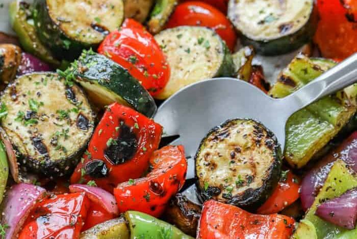 White bowl filled with grilled veggies with a spoon