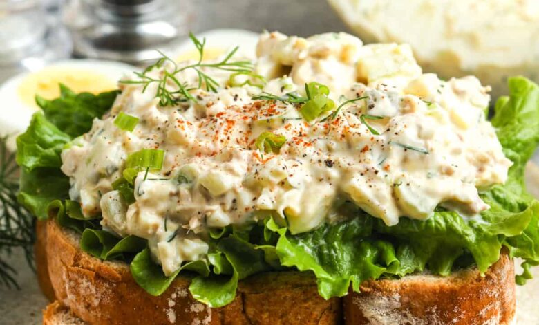 close up of a Tuna Egg Salad sandwich on a plate with bowl full of salad in the back