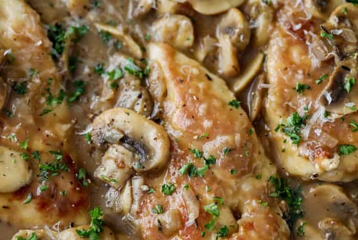 Chicken Marsala in a pan with mushrooms, parsley and shredded parmesan shown close up