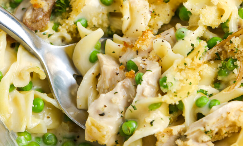 Serving chicken noodle casserole from a baking dish with a silver serving spoon