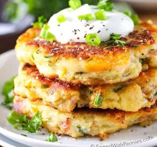 Loaded Mashed Potato Cakes with sour cream and green onions and parsley in the background on a wood table