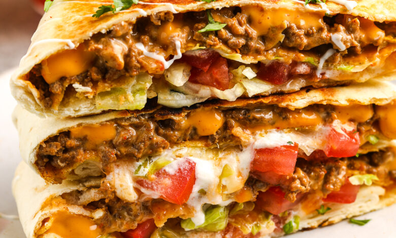 Crunchwrap Supreme stacked on a plate with diced tomatoes and cilantro