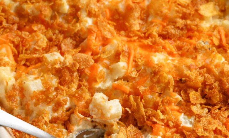 cooked Funeral Potatoes in a white casserole dish with a spoon taking a portion out