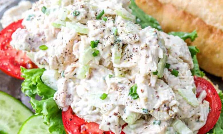 A classic chicken salad on a roll with tomatoes and lettuce next to cucumbers.